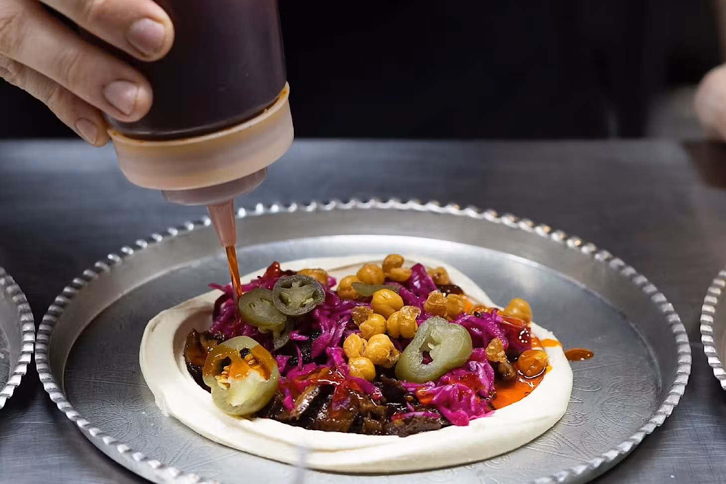 Someone squeeze some sauce onto a stacked tray of hummus.